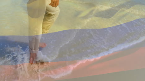 Animation-of-flag-of-colombia-over-biracial-woman-walking-at-beach
