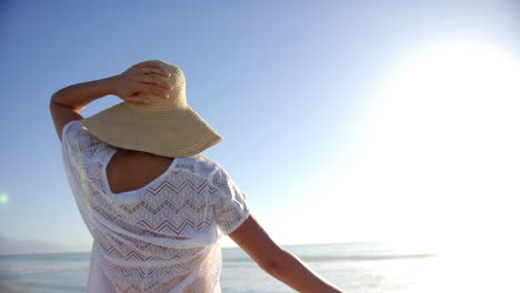 Young-biracial-woman-enjoys-the-beach-with-copy-space,-shielding-her-eyes-with-a-wide-brimmed-hat