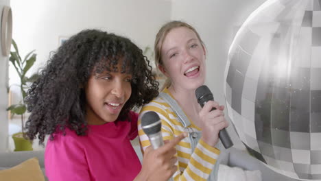 Animation-of-mirror-ball-over-happy-diverse-teenage-girls-with-microphones-singing-karaoke-at-home