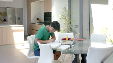 Teenage-Asian-boy-studying-on-a-laptop-at-a-modern-home-kitchen-table