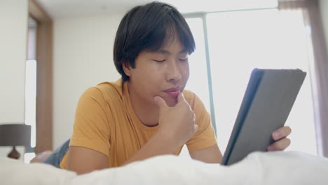 Teenage-Asian-boy-focused-on-a-tablet-at-home