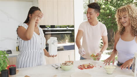 Young-Asian-man-and-biracial-women-laugh-in-a-home-kitchen-while-making-pizza