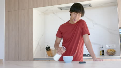 Teenage-Asian-boy-pours-milk-into-a-bowl-of-cereal-at-home,-with-copy-space