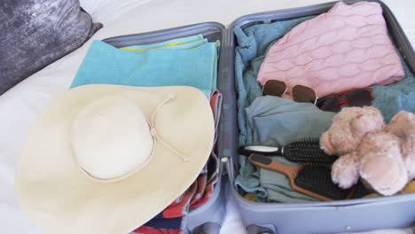 A-suitcase-is-open,-revealing-neatly-packed-clothes-and-a-teddy-bear