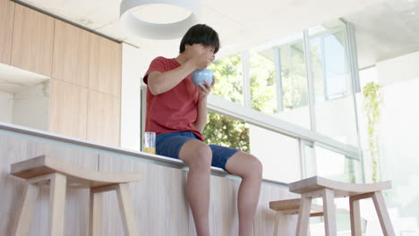 Teenage-Asian-boy-enjoys-a-bowl-of-cereal-at-a-modern-home-kitchen