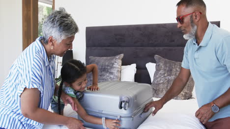 Biracial-grandparents-with-their-granddaughter-unpack-a-suitcase-on-a-bed