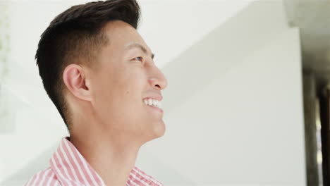A-young-Asian-man-smiles-brightly-at-home-in-a-well-lit-space,-with-copy-space