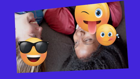 Animation-of-various-emojis-moving-over-two-happy-diverse-teenage-girls-lying-on-backs-talking
