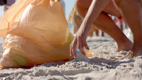 Diverse-volunteers-collect-trash-on-a-sandy-beach,-with-copy-space