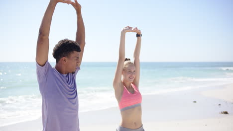 Young-biracial-man-and-Caucasian-woman-stretch-on-a-sunny-beach