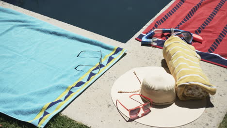 Sunglasses,-a-hat,-and-towels-are-beside-a-pool,-suggesting-a-leisurely-day