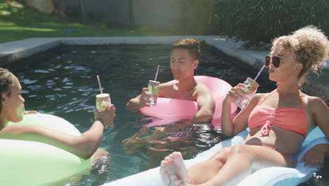 Young-Asian-man-and-two-biracial-women-enjoy-drinks-in-a-pool