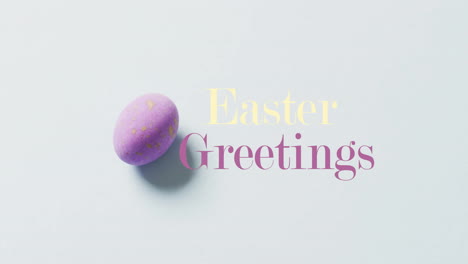 Animation-of-happy-greetings-text-over-purple-easter-egg-on-bue-background