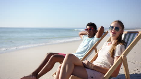 Young-biracial-man-and-young-Caucasian-woman-relax-on-beach-chairs-by-the-sea