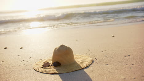 A-straw-hat-and-sunglasses-rest-on-a-sandy-beach,-bathed-in-sunlight,-with-copy-space