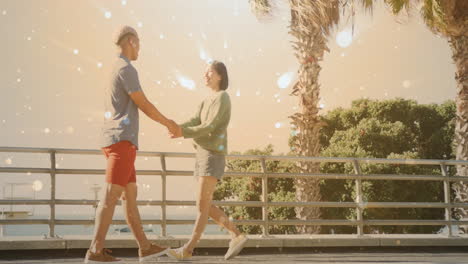 Animation-of-spot-lights-over-happy-diverse-couple-holding-hands-walking-by-sea