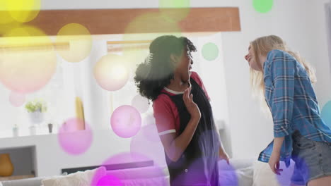 Animation-Von-Bunten-Lichtpunkten-über-Zwei-Unterschiedlichen-Teenager-Mädchen,-Die-Zu-Hause-Tanzen