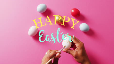Animation-of-happy-easter-text-over-biracial-woman-painting-colourful-easter-eggs-on-pink-background
