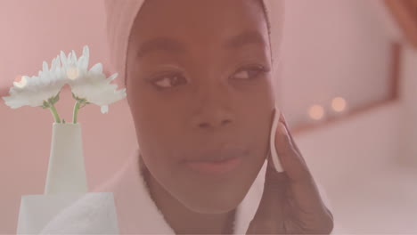 Animation-of-white-flowers-in-vase-over-happy-african-american-woman-cleansing-face-in-bathroom