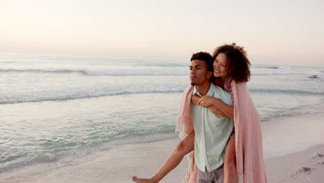 Biracial-couple-enjoys-a-serene-beach-at-sunset,-with-the-woman-embracing-the-man-from-behind,-with-