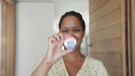 Young-biracial-woman-shows-a-'vote'-badge-at-home,-with-copy-space