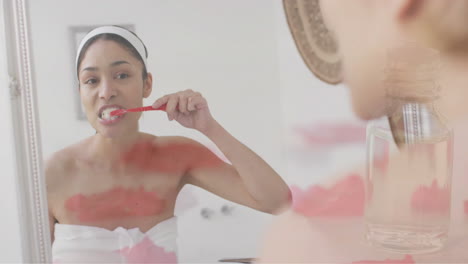 Animation-of-floating-rose-petals-over-biracial-woman-brushing-teeth-in-bathroom