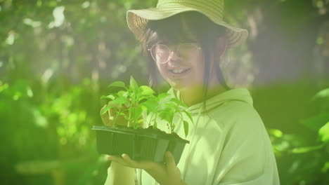 Animation-of-forest-over-happy-asian-girl-holding-plant