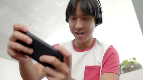 Teenage-Asian-boy-plays-a-game-on-his-smartphone-at-home,-fully-engaged