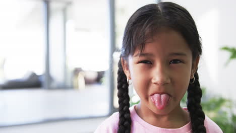 Biracial-girl-with-dark-hair-in-braids-sticks-out-her-tongue-playfully,-with-copy-space