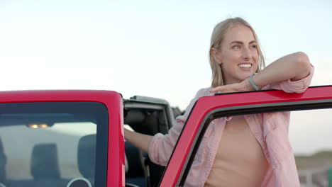 Young-Caucasian-woman-leans-on-a-red-car-door-on-a-road-trip,-with-copy-space