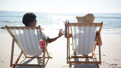 Young-biracial-man-and-young-Caucasian-woman-relax-on-beach-chairs,-holding-hands