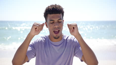 Young-biracial-man-with-short-curly-hair-celebrates-at-the-beach