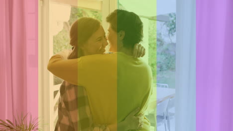 Animation-of-pride-rainbow-stripes-over-happy-caucasian-lesbian-couple-embracing-at-home