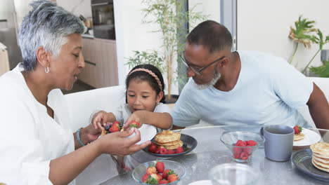 Biracial-girl-enjoys-breakfast-with-her-grandparents,-a-biracial-woman-and-man