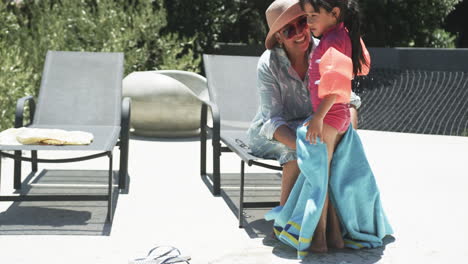 Biracial-woman-wraps-a-child-in-a-towel-poolside,-both-smiling-warmly