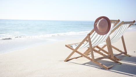 A-single-deck-chair-with-green-and-white-stripes-and-a-brown-hat-rests-on-a-sandy-beach-with-copy-sp