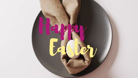 Animation-of-happy-easter-text-over-white-easter-egg-in-cloth-on-black-plate-on-white-background