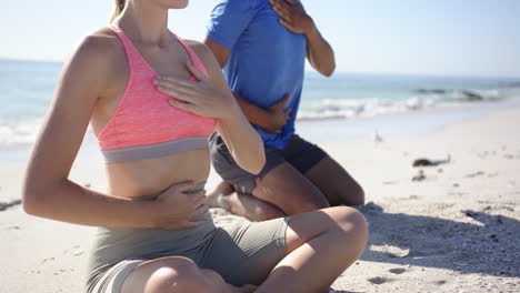Young-Caucasian-woman-and-biracial-man-meditate-on-a-sunny-beach