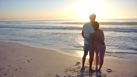 Biracial-couple-embraces-while-watching-a-beach-sunset-with-copy-space
