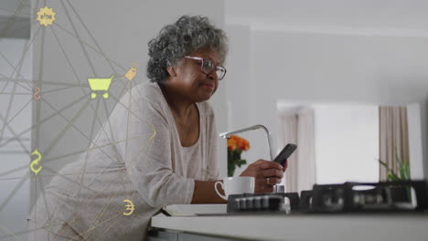Animation-of-network-of-connections-with-icons-over-senior-african-american-woman-using-smartphone
