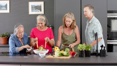 Senior-diverse-group-of-women-prepare-a-meal-together-in-a-home-kitchen,-including-a-salad
