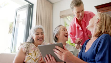 Senior-diverse-group-of-women-share-a-laugh-together-at-home-using-a-tablet