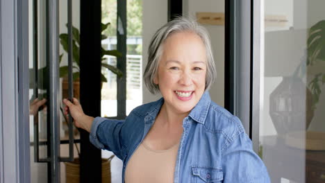 Senior-Asian-woman-with-grey-hair-smiles-warmly,-wearing-a-denim-shirt