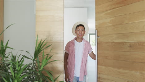Young-Asian-man-stands-smiling-at-the-entrance-of-a-modern-home