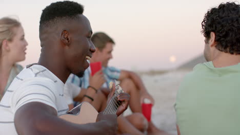 Young-African-American-man-plays-guitar-at-a-beach-gathering-at-a-party