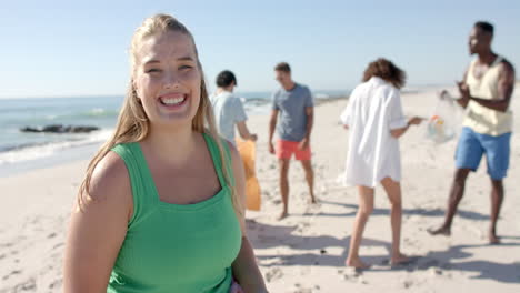 Young-Caucasian-woman-smiles-at-the-beach-while-collecting-trash,-with-copy-space