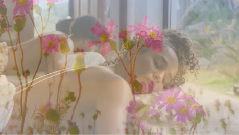 Animation-of-pink-flowers-in-garden-over-biracial-woman-lying-on-massage-table