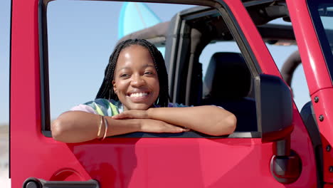 Young-African-American-woman-leans-on-a-red-car-door-on-a-road-trip