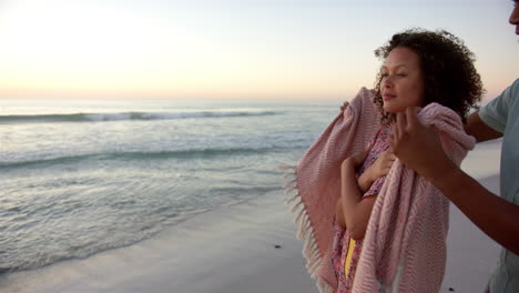 Biracial-couple-enjoys-a-serene-beach-sunset,-wrapped-in-a-cozy-blanket,-with-copy-space