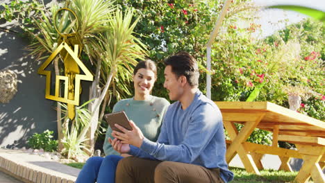 Animation-of-gold-house-key-and-key-fob-over-happy-diverse-couple-using-tablet-in-garden-at-home
